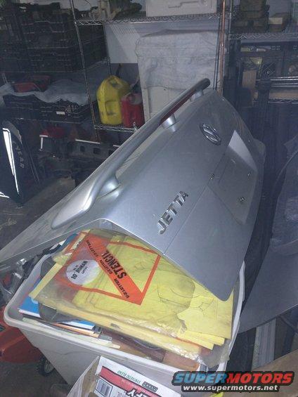 Silver Volkswagen Jetta trunk lid with 'JETTA' badge, sitting on top of a bin of stencils