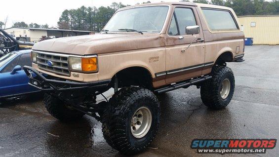 Lifted Ford Bronco with big tires and custom bumper parked next to a blue car