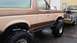 1988 Ford Bronco - A lifted Ford Bronco with a two-tone paint job sits beside an older, weathered pickup truck.