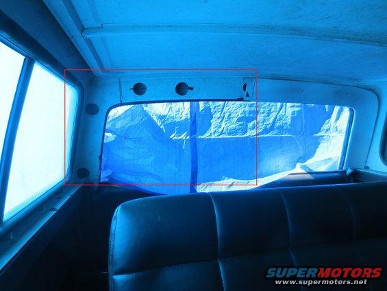 Rear interior of a vehicle, looking out the back window covered by a blue tarp. Seats are visible