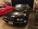 1988 BMW 7 Series - A black BMW sedan is parked in a garage, with a red classic car visible to its left.