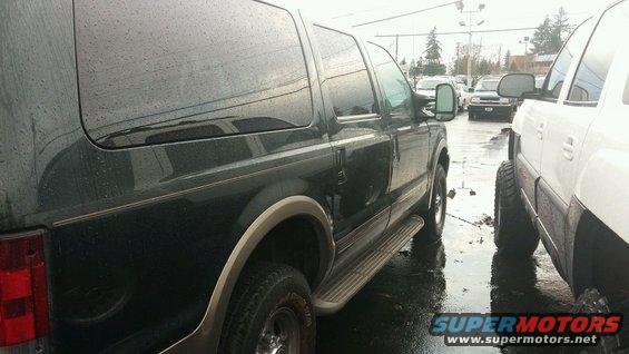 Dark green 2003 Ford Excursion parked next to a white pickup truck on a wet day