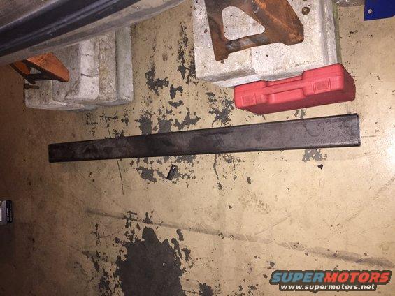 Metal bar, red toolbox, and jack stands on a dirty garage floor