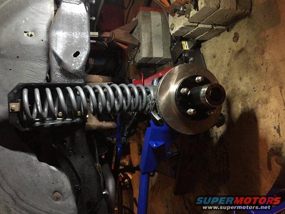 Front suspension assembly with coil spring and brake rotor, supported by a blue jack stand