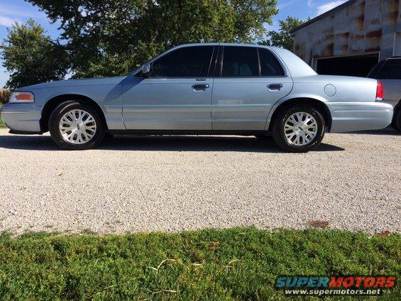 Light blue 2003 Ford Crown Victoria parked on gravel lot next to a building