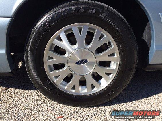 Close-up of a silver Ford wheel with a blue Ford logo on a light blue car