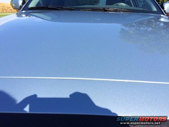 Blue car hood with a thin white line across it. Shadow of a person is visible