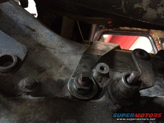Close-up of transmission linkage with a Ford logo visible on the casing. A red interior is visible in the background