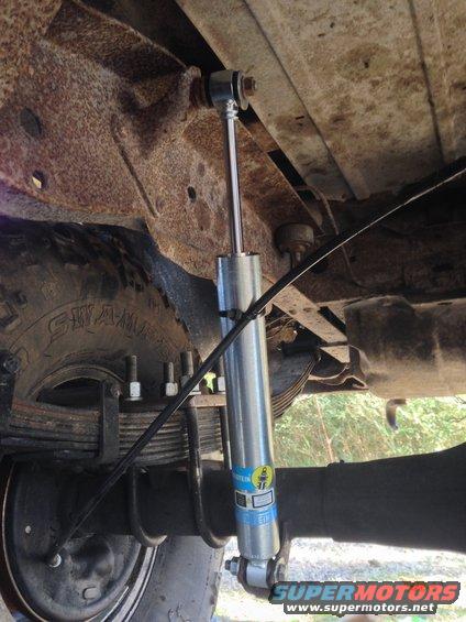 Rear suspension of a vehicle showing a Bilstein shock absorber, leaf springs, and part of a tire. The frame is heavily rusted