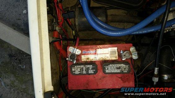 Red Duracell battery in a vehicle engine bay with blue hoses and red wiring