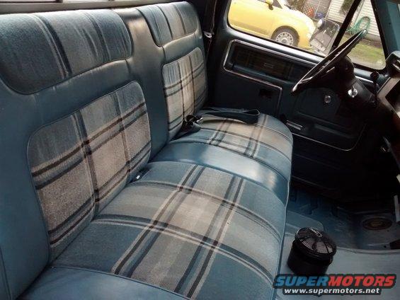 Interior shot of a truck's bench seat with plaid inserts. A yellow car is visible through the window