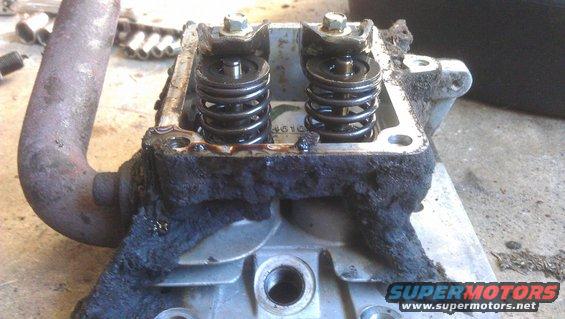 Engine cylinder head with visible valves and springs, covered in grime