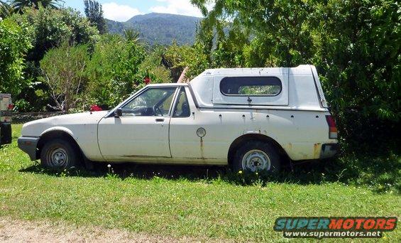 White pickup truck with a white camper shell parked on grass, showing rust spots and a fuel cap