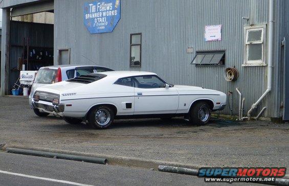 White coupe with louvred rear window and side vents parked next to a silver hatchback