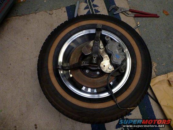 Tire with whitewall and chrome rim, attached to a brake caliper and rotor assembly