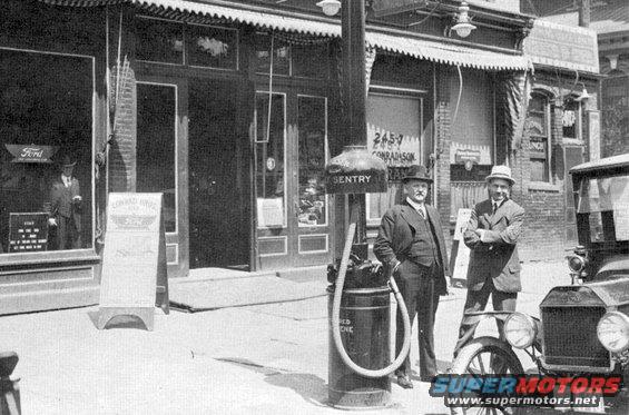 1915 Ford Model T front view, black and white photo, parked on street with two men and gas pump