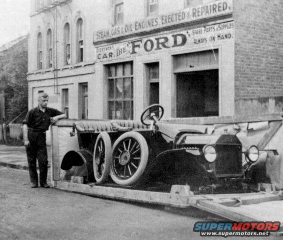 1915 Ford Model T on a trailer in front of a Ford service building. Man stands next to the trailer