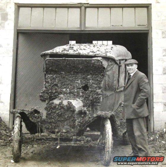 1915 Ford Model T covered in mud, standing in a doorway with a man beside it