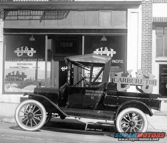 Black 1915 Ford Model T truck with a canvas top, parked in front of a storefront