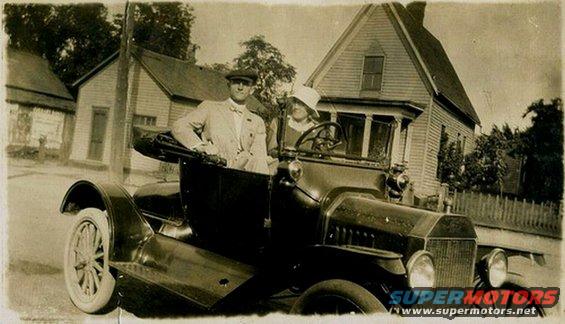 1915 Ford Model T with two people in it, parked in front of a house