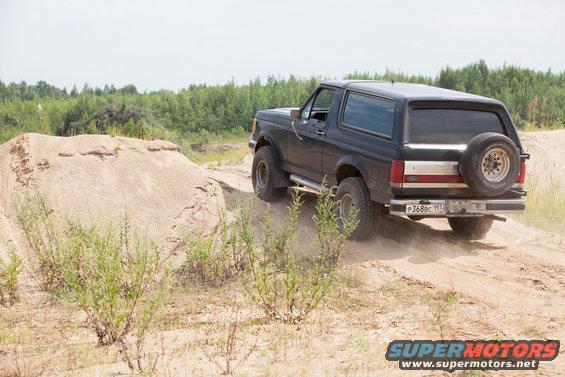 1987 Ford Bronco rear view, black, with spare tire on back, driving on dirt