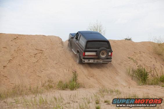 Black 1987 Ford Bronco driving up a sandy hill