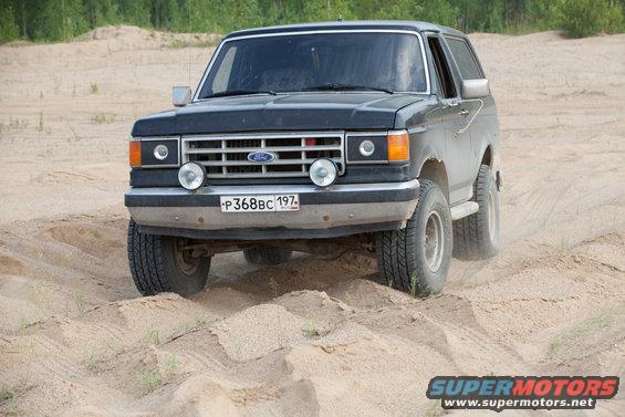 Black 1987 Ford Bronco driving on sand, front 3/4 view