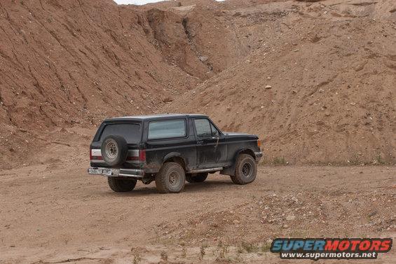 Black 1987 Ford Bronco with spare tire on back, parked on dirt road