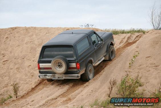 1987 Ford Bronco driving up a sand dune, rear view. License plate reads P368BC 193