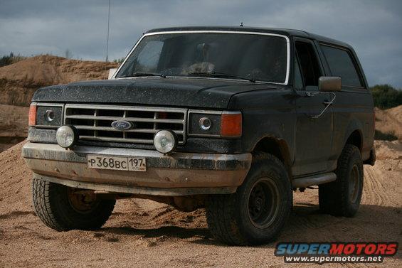 Black Ford Bronco parked on a dirt road with sand piles in the background