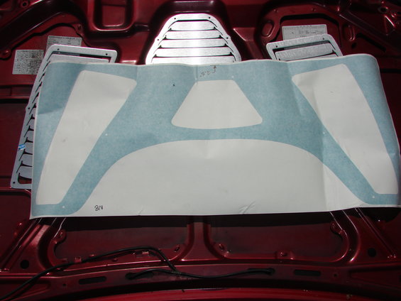 Red car hood interior with silver louvers and a white sticker template with blue masking