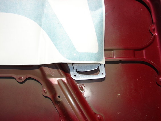 Red metal hood interior with a silver latch mechanism and a partial white sticker with blue trim