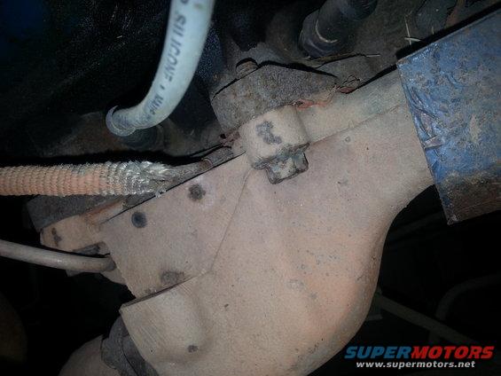 Close-up of engine exhaust manifold with a silicone hose above it. Some braided material is visible