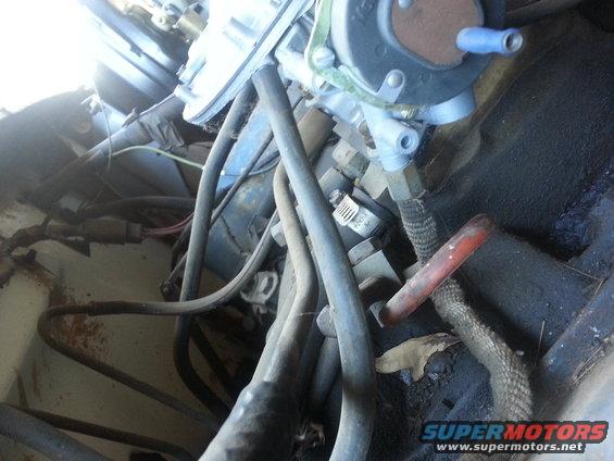 Engine bay close-up showing carburetor, fuel lines, and various hoses. Some rust is visible