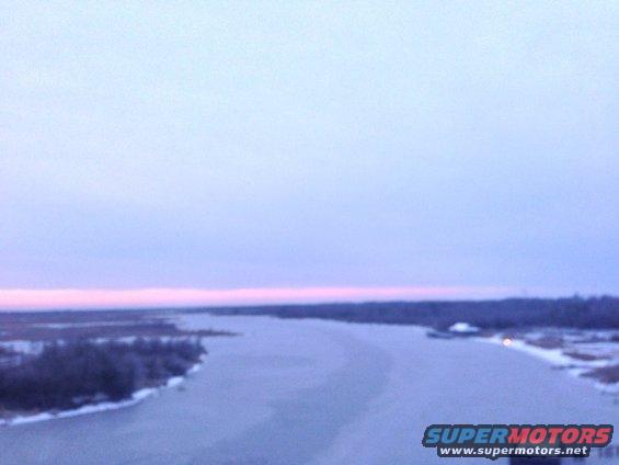 Frozen river and snow-covered banks under a pale pink and blue sky