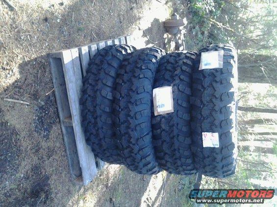 Four large off-road tires stacked on a wooden pallet outdoors