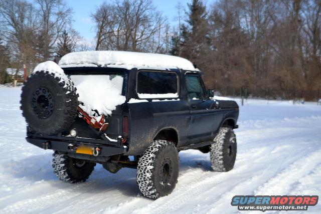 Black SUV with spare tire on rear, covered in snow, driving in a snowy field