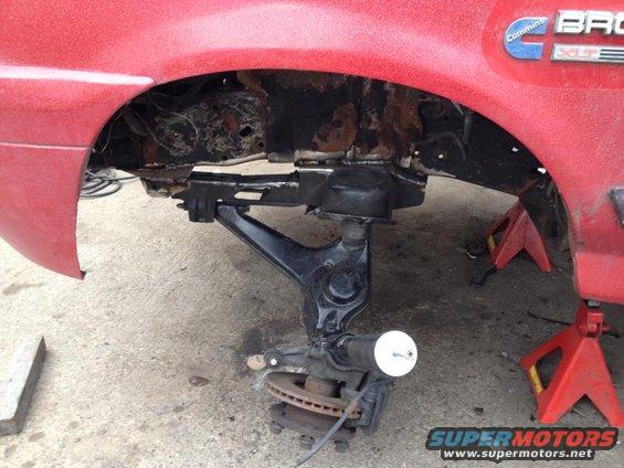 Close-up of a vehicle's suspension components, including a control arm and brake rotor, supported by jack stands