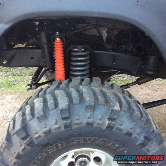 Close-up of a large off-road tire and suspension components, including an orange shock absorber and coil spring