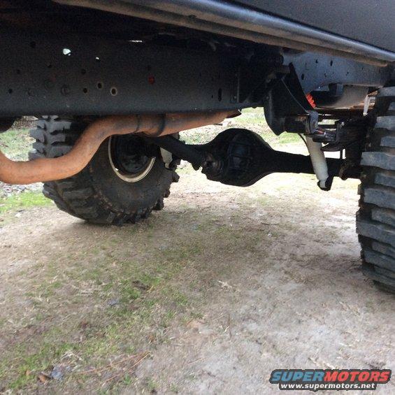Undercarriage of a lifted vehicle showing a large tire, exhaust pipe, and rear axle