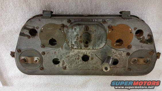 Rear view of a rusty, metal dashboard instrument cluster with multiple circular openings and mounting points
