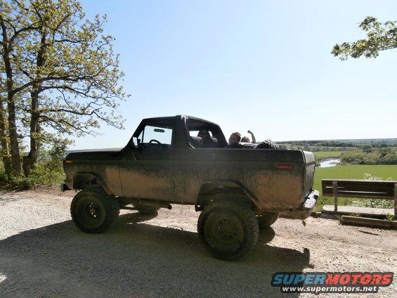 Mud-covered black 1978 Ford Bronco with a lifted suspension and off-road tires parked on a gravel road