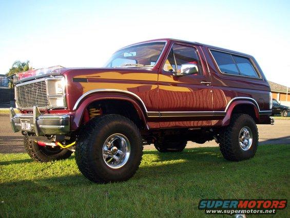 Maroon Ford Bronco with yellow trim, lifted suspension, and chrome wheels parked on grass