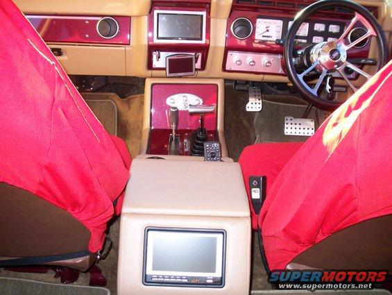 1985 Ford Bronco interior with red seat covers, aftermarket steering wheel, and multiple screens