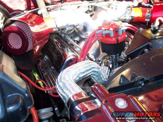 Engine bay detail showing red air filter, distributor cap with red spark plug wires, and chrome accents