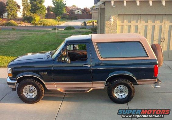 Dark blue and tan Ford Bronco SUV parked on a driveway, side view. Spare tire mounted on the rear