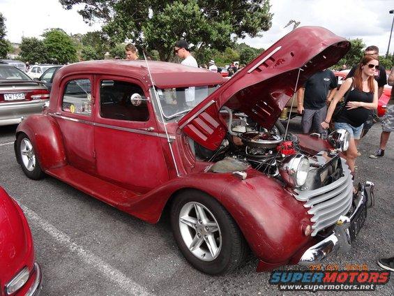 Red vintage car with hood open, showing engine. People standing around it