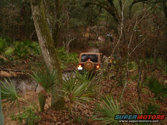 Tan Jeep Wrangler on a muddy trail, rear view