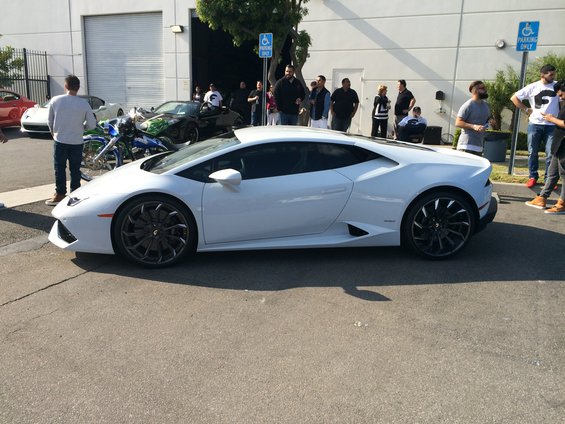 White Lamborghini Huracan parked on asphalt, with people and other vehicles in the background