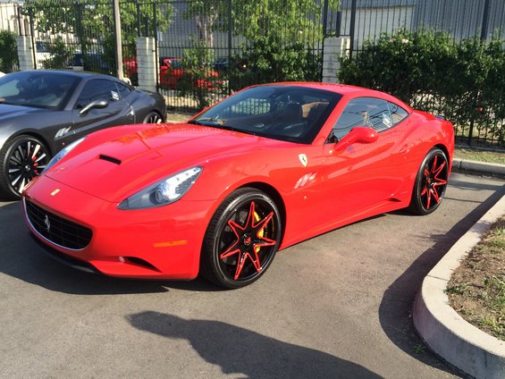 Red Ferrari California with custom black and red wheels parked next to a grey car